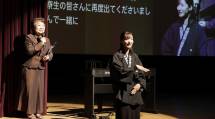 舞台上で司会者の言葉を伝える手話通訳者と、字幕が映し出されたスクリーン
